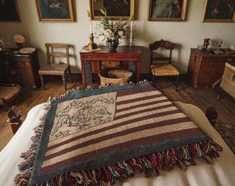 May include: A vintage-style American flag throw blanket with a woven eagle design in the center. The blanket is made of a soft, textured fabric and has a fringed edge.
