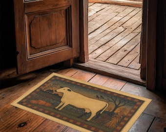 May include: Rectangular doormat featuring a cream-colored cow illustration on a dark green and brown background. The mat has a tan border and depicts pumpkins, trees, and a starry sky. Placed in an open doorway on a wooden floor.
