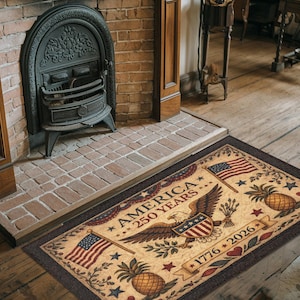 May include: Rectangular beige rug with a brown border, featuring an American flag, an eagle, pineapples, stars, and the text "AMERICA 250 YEARS 1776-2026". Decorative rug for a home.