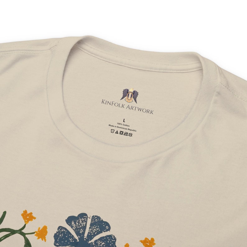 May include: A white t-shirt with a floral print and a label that says "Kinfolk Artwork" with a logo of a bird with wings spread. The label also says "100% Cotton" and "Made in Dominican Republic".