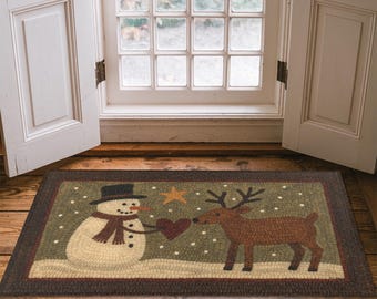 May include: A rectangular rug with a snowman and reindeer design. The snowman, wearing a black hat and scarf, offers a heart to the reindeer. The rug has a brown border and a green background with a star and snowflakes, suitable for a doorway.