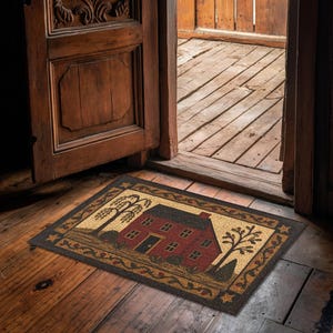 May include: A rectangular doormat featuring a red house with a black roof and door, set against a tan background. The house is flanked by stylized trees and surrounded by a decorative border. The mat is placed in front of a wooden door.