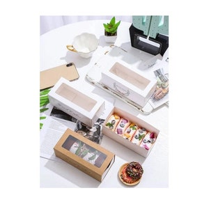 May include: Three white cardboard boxes with clear plastic windows for displaying baked goods. The boxes have a floral design and the text "Sweet Wishes" printed on them. One box is filled with a pastry topped with fruit and whipped cream.