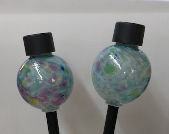 May include: Two glass globe solar lights with black metal stakes. The globes are clear and have a white, blue, green, and purple speckled pattern.