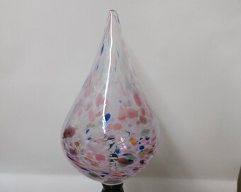 May include: A clear glass teardrop-shaped ornament with pink, blue, and white confetti-like inclusions. The ornament is attached to a black metal rod.