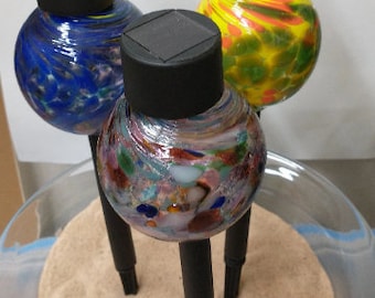 May include: Three glass globe solar lights with black tops. The globes are filled with colorful swirls of glass. The lights are sitting on a bed of sand in a clear glass bowl.