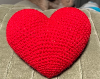 May include: A red crocheted heart-shaped pillow on a green couch.