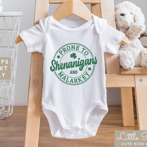 May include: White baby onesie with a green circle graphic that says "Prone to Shenanigans and Malarkey".