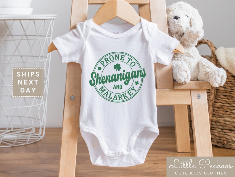 May include: White baby onesie with a green circle graphic that says "Prone to Shenanigans and Malarkey".