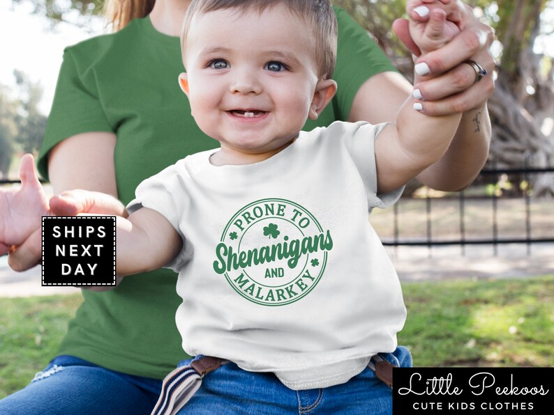 May include: White baby onesie with a green circle graphic that says "Prone to Shenanigans and Malarkey".