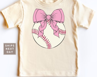 Puede incluir: Una camiseta de color crema con un lazo rosa encima de un gráfico de béisbol.