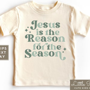 May include: A cream colored t-shirt with a green and blue graphic that says "Jesus is the Reason for the Season".