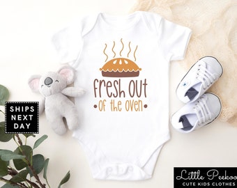 May include: White baby onesie with a brown pie and the text "fresh out of the oven".