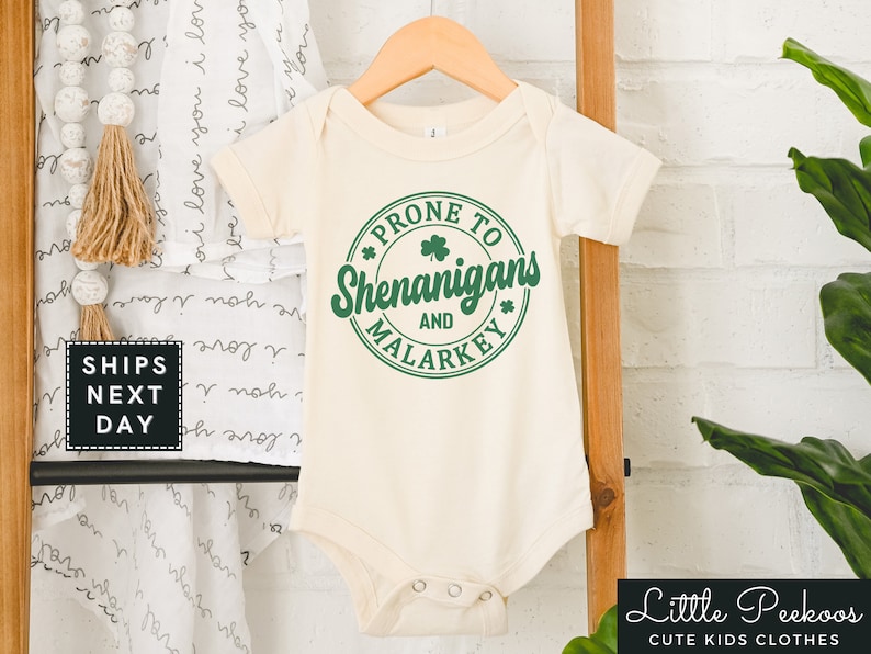 May include: A white baby onesie with a green circle graphic that says "Prone to Shenanigans and Malarkey".