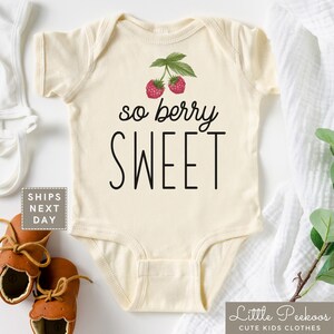 May include: A cream-colored baby onesie with the text "so berry sweet" in black. Two red raspberries with green leaves are above the text.