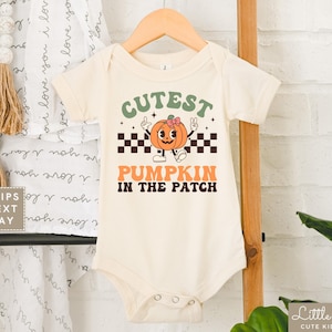 May include: A white baby onesie with a green, orange, and black graphic of a pumpkin with the text "Cutest Pumpkin in the Patch".