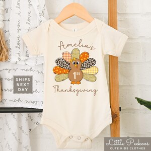 May include: A white onesie with a brown turkey graphic and the text "Amelia's 1st Thanksgiving".