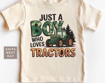 May include: A cream-colored t-shirt featuring the text "JUST A BOY WHO LOVES TRACTORS" with a green camouflage-patterned "BOY" and a green tractor graphic. The shirt is designed for children.