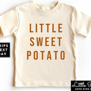 May include: A cream colored short-sleeved t-shirt with the words "LITTLE SWEET POTATO" printed in brown on the front.