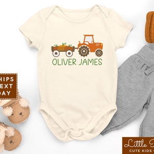 May include: A white baby onesie with a green and orange tractor pulling a wagon full of pumpkins. The onesie has the name "Oliver James" printed on it.