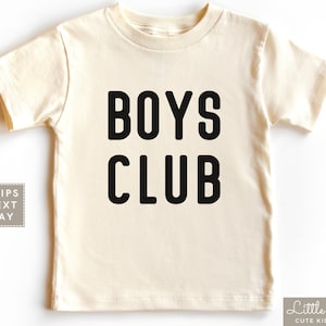 May include: A cream colored short-sleeved t-shirt with the text "BOYS CLUB" printed in black.