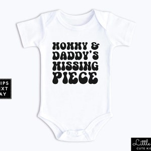 May include: White baby onesie with black text that reads "Mommy & Daddy's Missing Piece" in a retro font.