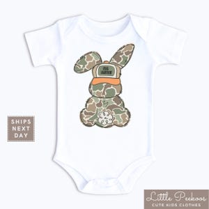 May include: White baby onesie with a camouflage bunny wearing an orange hat that says "egg hunter".