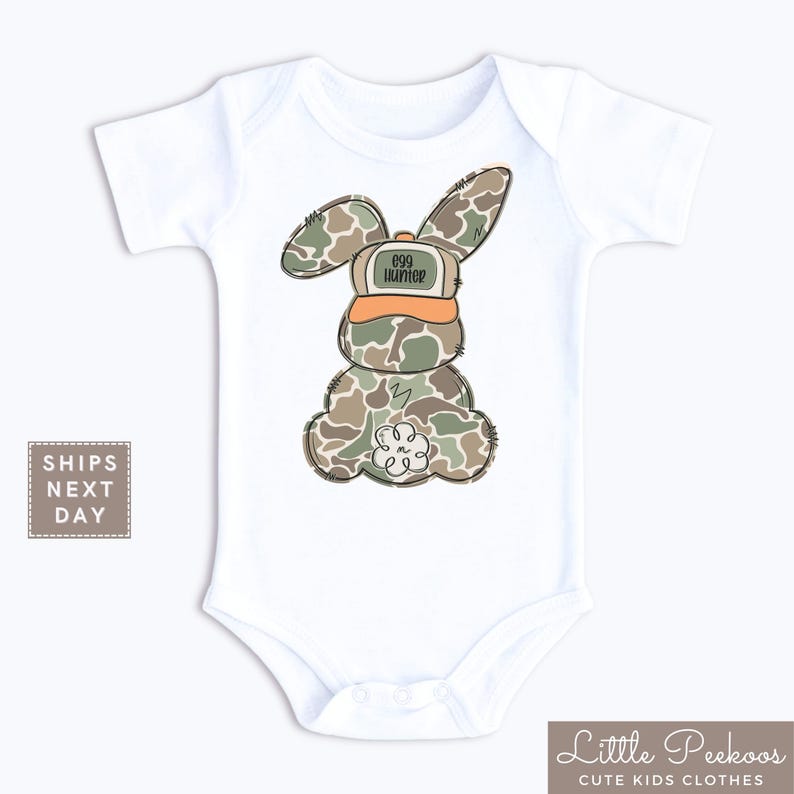 May include: White baby onesie with a camouflage bunny wearing an orange hat that says "egg hunter".