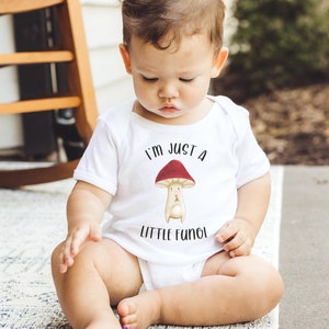 May include: A white baby onesie with a red and white mushroom graphic and the text "I'm just a little fungi".