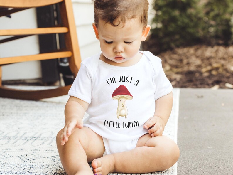 May include: A white baby onesie with a red and white mushroom graphic and the text "I'm just a little fungi".