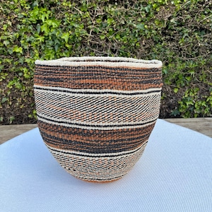 May include: A large, woven storage basket with a brown, black and white striped pattern. The basket is made of natural fibres and has a rounded shape.
