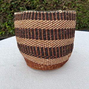 May include: A woven basket with a brown, black and white striped pattern. The basket is made from natural materials and has a round shape.
