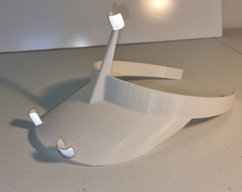 May include: White plastic visor with two small, curved, white plastic arms extending from the sides. The visor is designed to be worn on the head.
