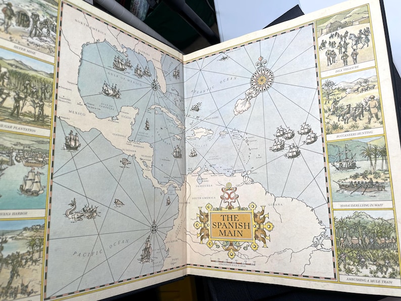 Puede incluir: Libro abierto con un mapa antiguo del Caribe, titulado "The Spanish Main". El mapa presenta ilustraciones de barcos, escenas hist&oacute;ricas y una rosa de los vientos. La paleta de colores incluye azules, beiges y amarillos.