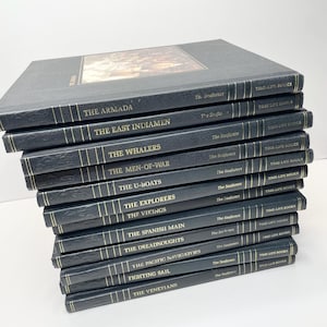 Puede incluir: Una pila de libros Time-Life de la serie "Seafarers". Los libros tienen cubiertas azul oscuro con letras doradas. Los t&iacute;tulos incluyen "The Armada", "The East Indiamen" y "The Whalers". El libro superior presenta una imagen en color.