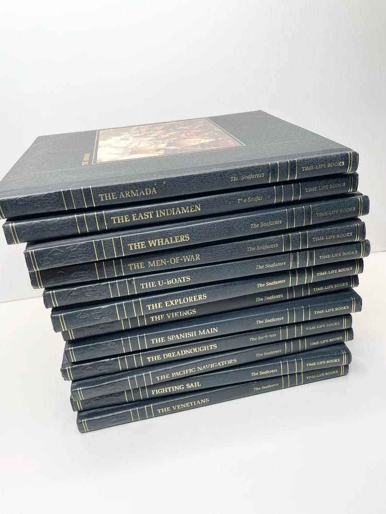 Puede incluir: Una pila de libros Time-Life de la serie "Seafarers". Los libros tienen cubiertas azul oscuro con letras doradas. Los t&iacute;tulos incluyen "The Armada", "The East Indiamen" y "The Whalers". El libro superior presenta una imagen en color.