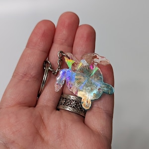 Könnte beinhalten: Ein Schlüsselanhänger in Form einer regenbogenfarbenen Meeresschildkröte mit einem silbernen Schlüsselring. Die Schildkröte ist aus Harz und hat eine glitzernde Oberfläche.