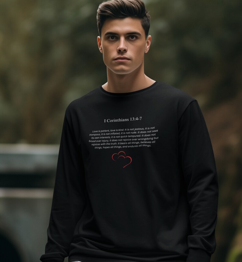 May include: Black long-sleeve sweatshirt with a white print of a Bible verse from 1 Corinthians 13:4-7. The verse is about love being patient, kind, and not jealous. The print also includes two red hearts.