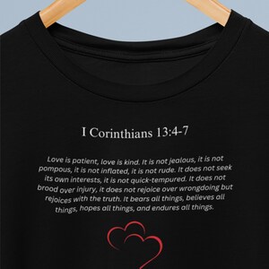May include: Black t-shirt with white text that reads "I Corinthians 13:4-7" and a quote about love. The quote reads "Love is patient, love is kind. It is not jealous, it is not pompous, it is not inflated, it is not rude. It does not seek its own interests, it is not quick-tempered. It does not brood over injury, it does not rejoice over wrongdoing but rejoices with the truth. It bears all things, believes all things, hopes all things, and endures all things."