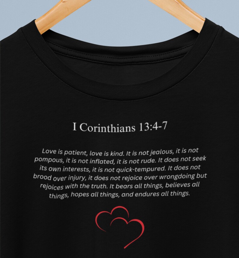 May include: Black t-shirt with white text that reads "I Corinthians 13:4-7" and a quote about love. The quote reads "Love is patient, love is kind. It is not jealous, it is not pompous, it is not inflated, it is not rude. It does not seek its own interests, it is not quick-tempered. It does not brood over injury, it does not rejoice over wrongdoing but rejoices with the truth. It bears all things, believes all things, hopes all things, and endures all things."