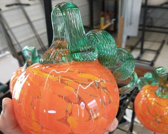 Può includere: Una zucca di vetro soffiata a mano con un motivo a spirale in arancio e giallo. La zucca ha un gambo di vetro verde.