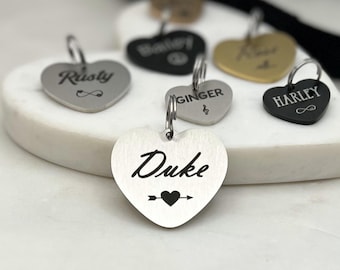 May include: A collection of silver heart-shaped pet ID tags with engraved names, including "Rusty", "Duke", "Ginger", and "Harley".