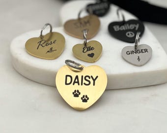 May include: A collection of gold heart-shaped dog tags with engraved names, including "Rose", "Elle", "Daisy", "Ginger", and "Bailey".