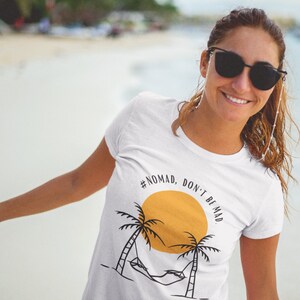 May include: White t-shirt with a graphic of a palm tree, hammock, and sun with the text "#NOMAD, DON'T BE MAD".