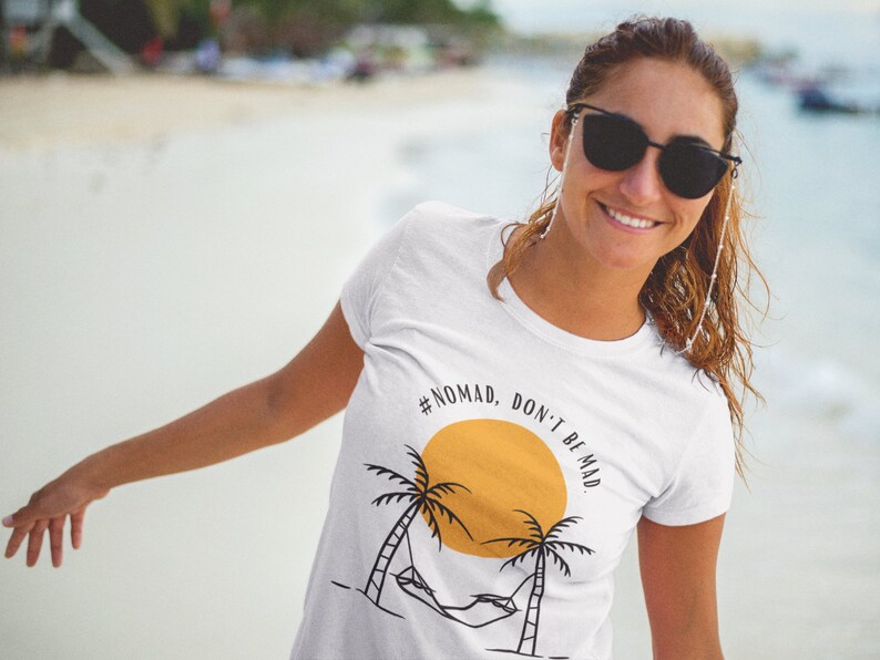 May include: White t-shirt with a graphic of a palm tree, hammock, and sun with the text "#NOMAD, DON'T BE MAD".