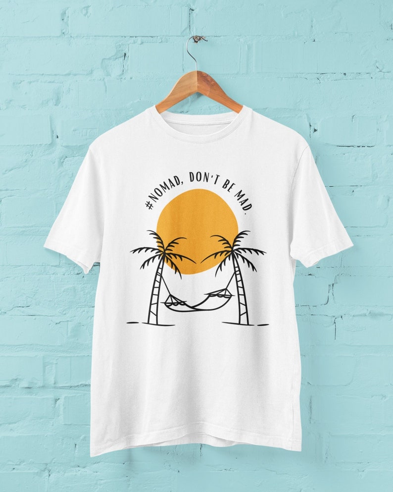 May include: White t-shirt with a black graphic design of palm trees, a hammock, and a yellow sun. The text '#NOMAD, DON'T BE MAD' is written in a black circle around the sun.