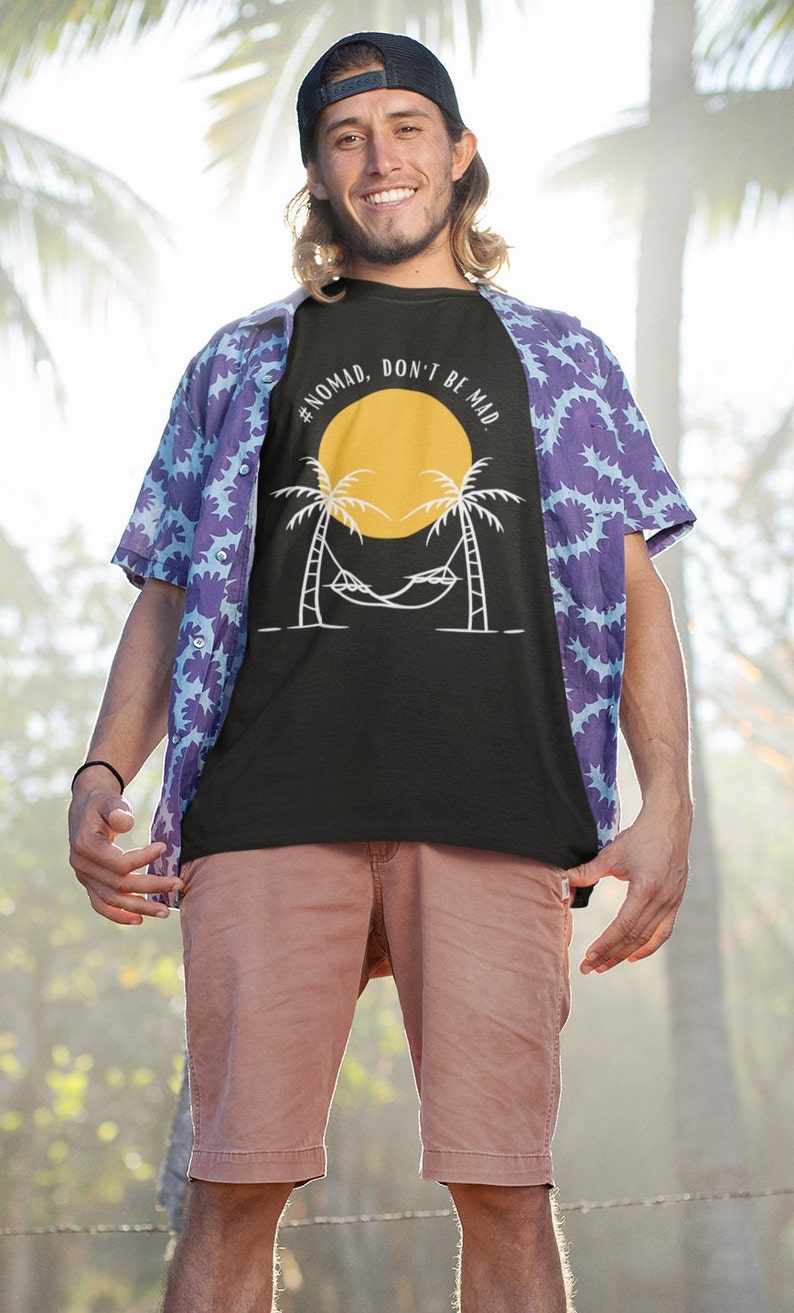 May include: A black t-shirt with a white graphic of a palm tree with a hammock and a yellow sun. The text on the shirt reads "#NOMAD, DON'T BE MAD."