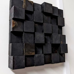 May include: A black wooden wall art piece made of stacked square blocks. The blocks are arranged in a staggered pattern, creating a textured and modern look.