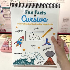 May include: A spiral bound notebook with a colorful cover featuring the words "Fun Facts in Cursive". The cover also includes a cursive letter "A" with a pencil pointing to it, a rocket ship, a wave, a volcano, and a parrot. The words "amazing", "earth", "super", "explosion", "awesome", and "octopus" are also on the cover.