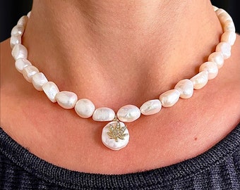 May include: A white pearl necklace with a gold pendant featuring a marijuana leaf design. The necklace is on a person's neck.